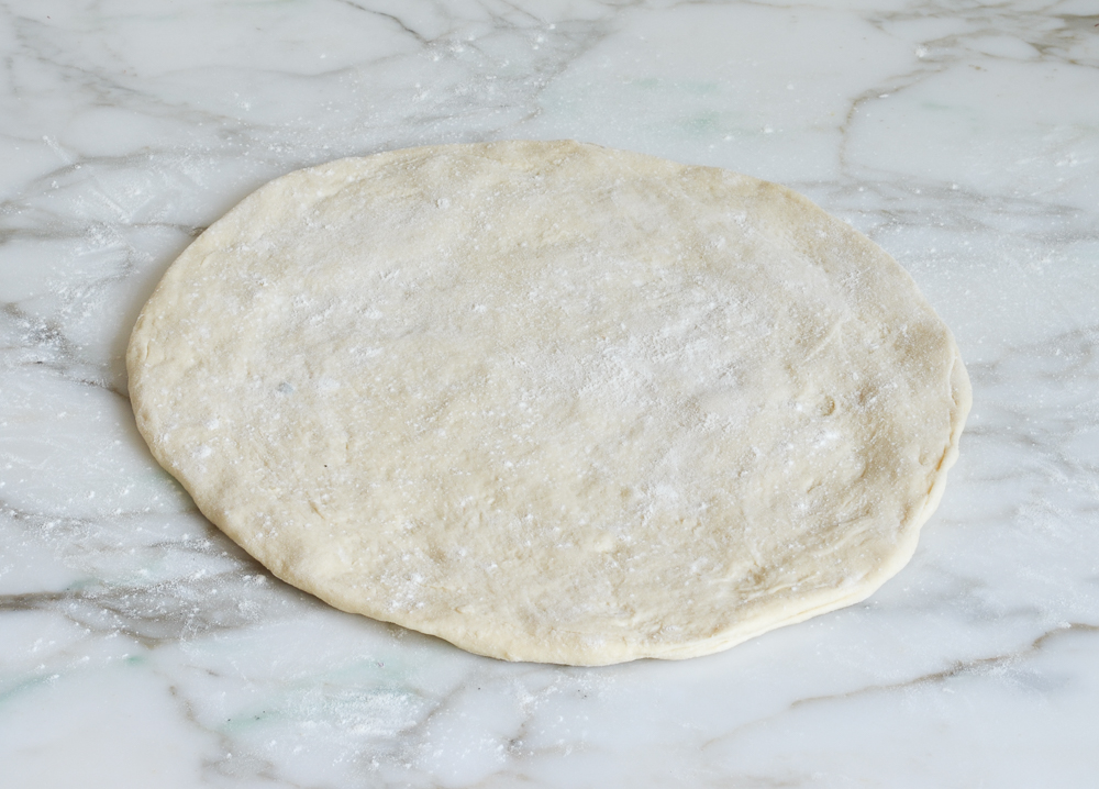 Circle of pizza dough on a marbled surface.
