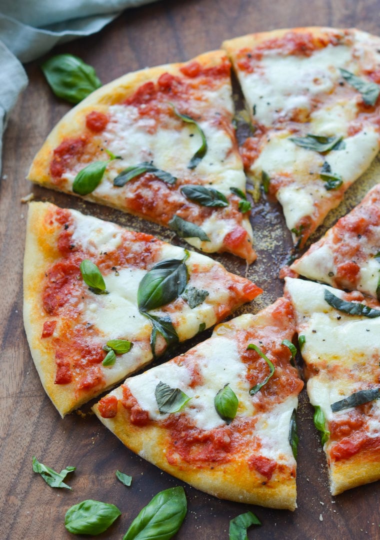 Sliced margherita pizza on a wooden cutting board.