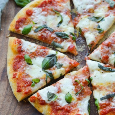 Sliced margherita pizza on a wooden cutting board.