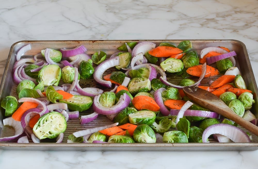 tossing the vegetables with oil and seasoning on the baking pan.