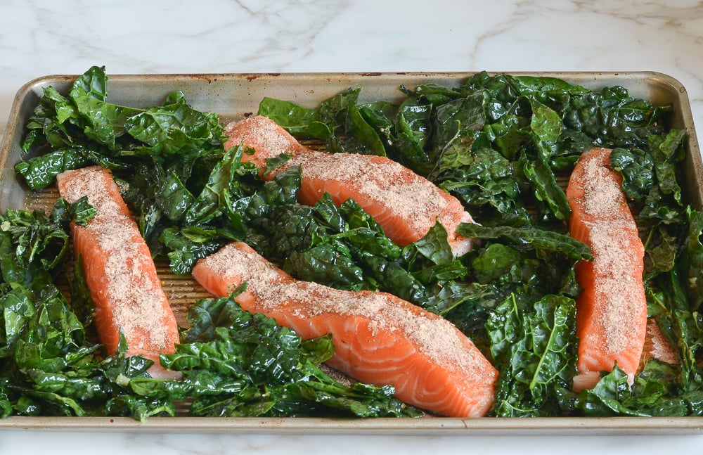 kale and salmon arranged on sheet pan ready to bake