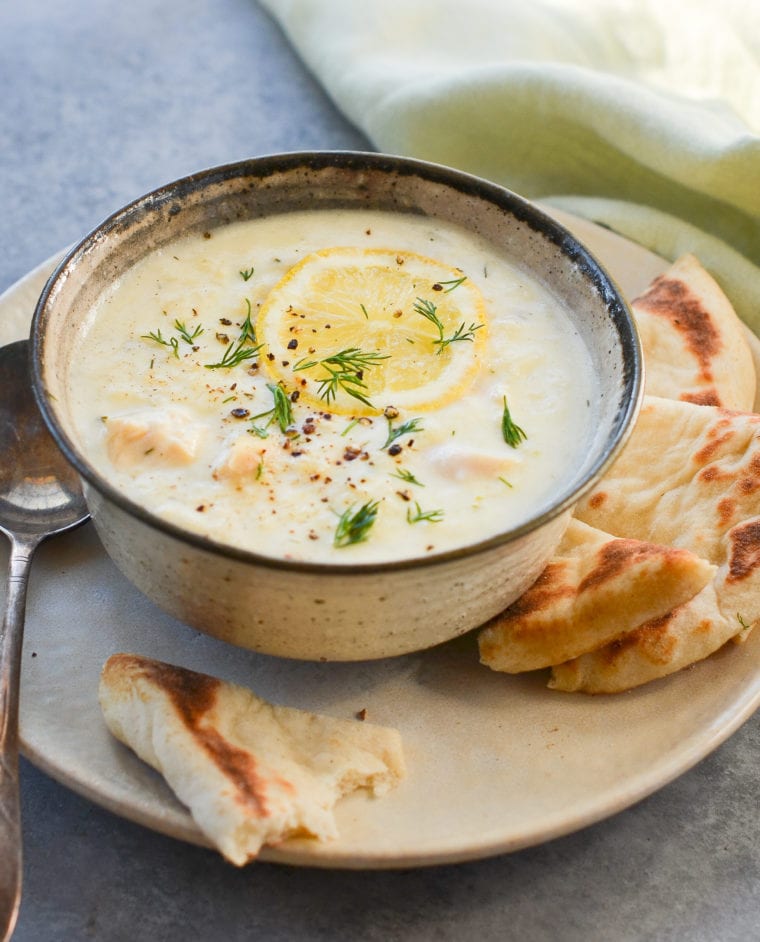 Bowl of avogolemono soup on a plate with bread.