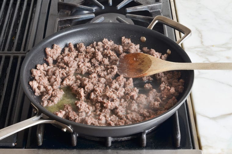 Wooden spoon in a skillet of browned beef.