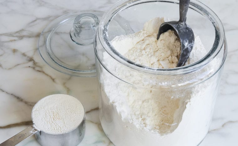 Leveled measuring cup of flour next to a glass container of flour.