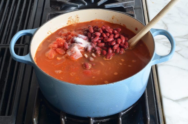 adding tomatoes and beans to the pot.