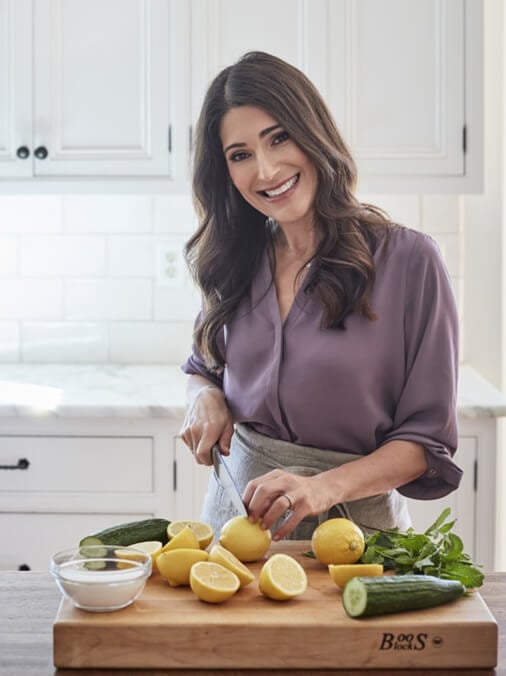 Jenn Segal standing at a counter, slicing lemons and smiling.