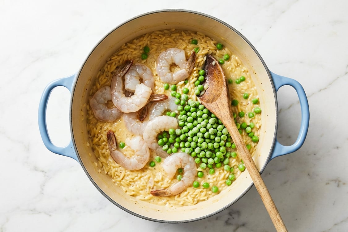 Shrimp and peas added to orzo risotto in Dutch oven.