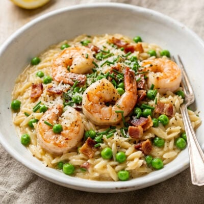Orzo risotto with shrimp, bacon, and peas in white ceramic bowl.