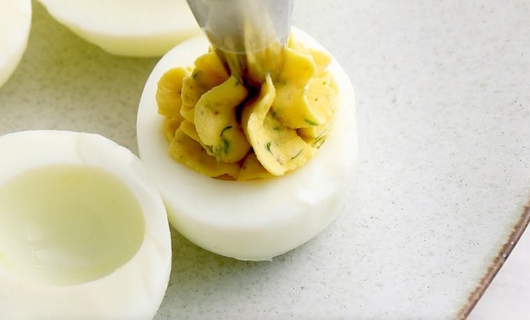 A pastry bag tip filling the deviled eggs on a plate.