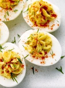 A plate of deviled eggs topped with paprika and herbs.