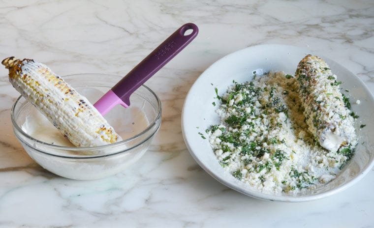spreading sauce on corn and coating with cotija and cilantro