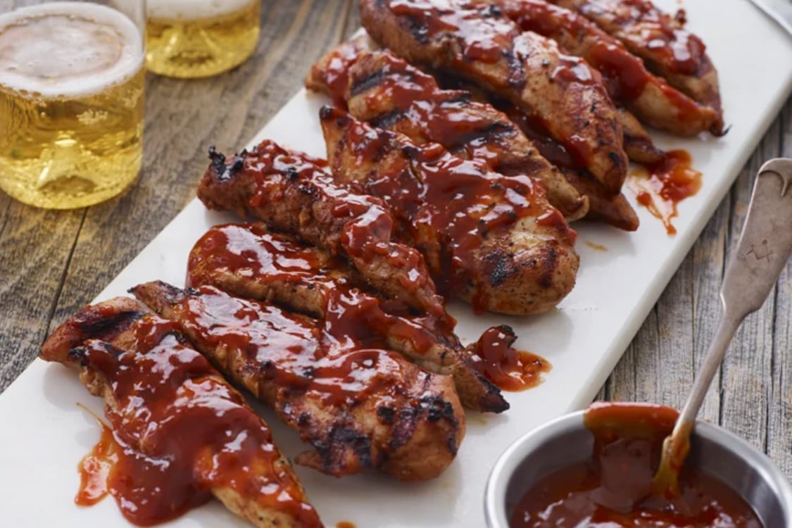 Grilled bbq chicken on picnic table with bowl of BBQ sauce and beer.