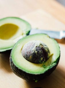 Halved avocado on a cutting board with a knife.