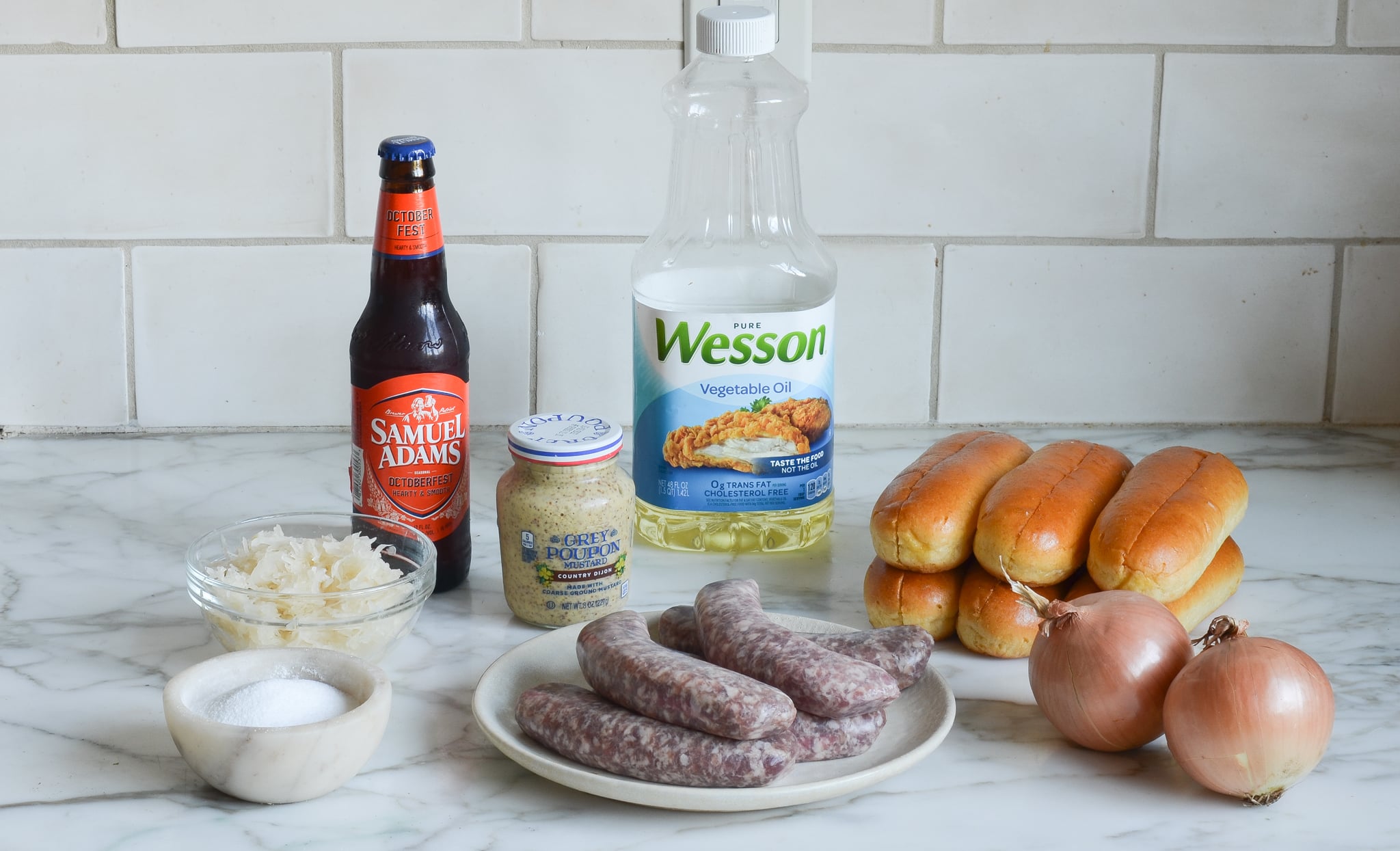 Bratwurst ingredients including Samuel Adams beer, vegetable oil, and onion on the counter.