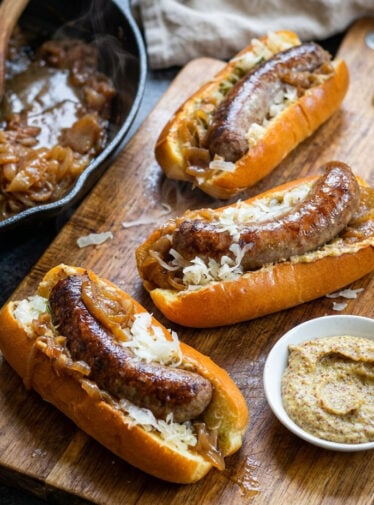 Beer brats on cutting board with bowl of mustard.