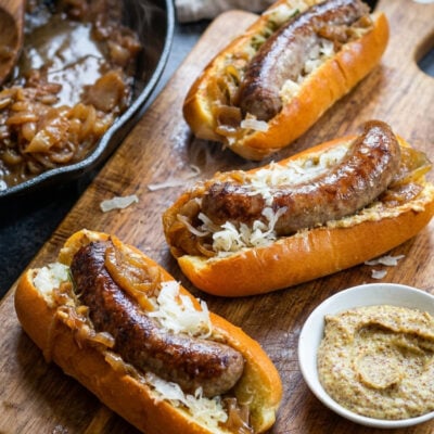 Beer brats on cutting board with bowl of mustard.