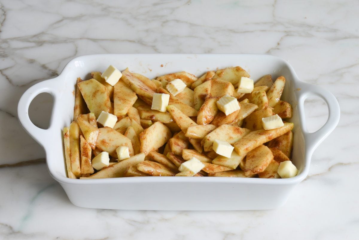 assembling apple cobbler with apples in baking dish dotted with butter