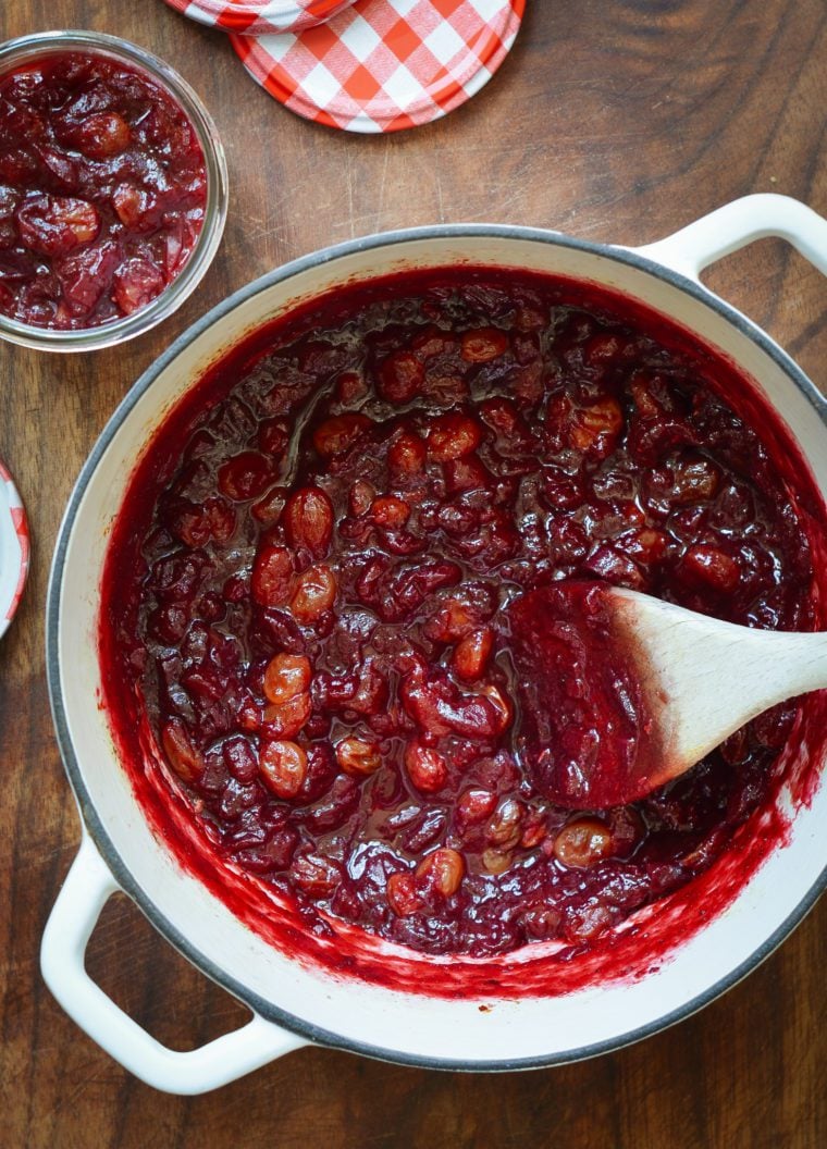 Wooden spoon stirring a Dutch oven of cranberry chutney.