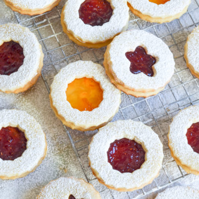 Linzer cookies with various shapes on and around a wire rack.