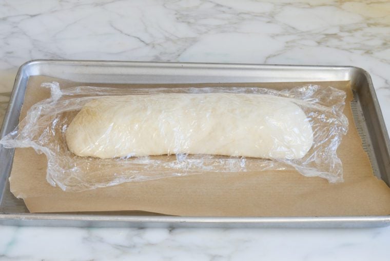Plastic-wrapped stromboli on a lined baking sheet.
