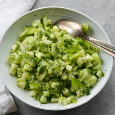 Spoon in a bowl of green apple and celery salad with dill.