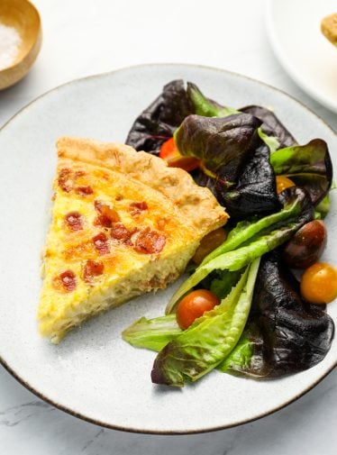 Slice of quiche Lorraine on a plate with a salad.