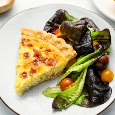 Slice of quiche Lorraine on a plate with a salad.