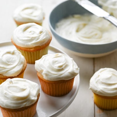 Vanilla cupcakes on and around a raised platter.