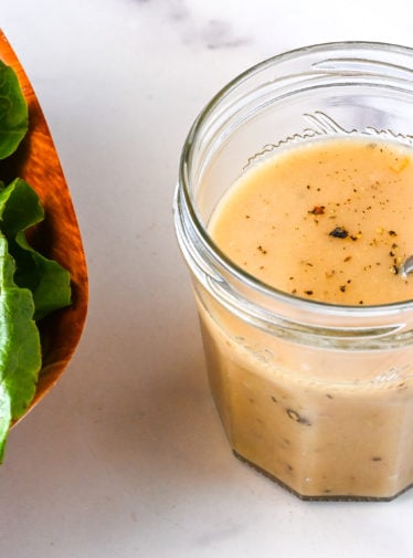 Glass jar of vinaigrette next to a bowl of salad.