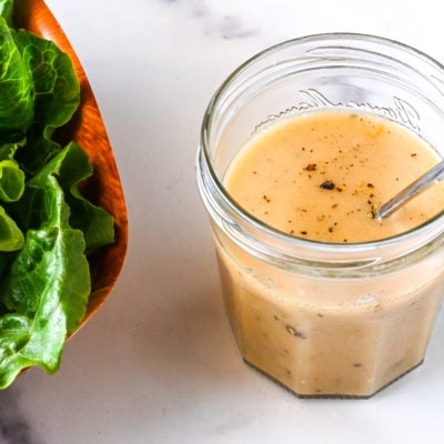 Glass jar of vinaigrette next to a bowl of salad.