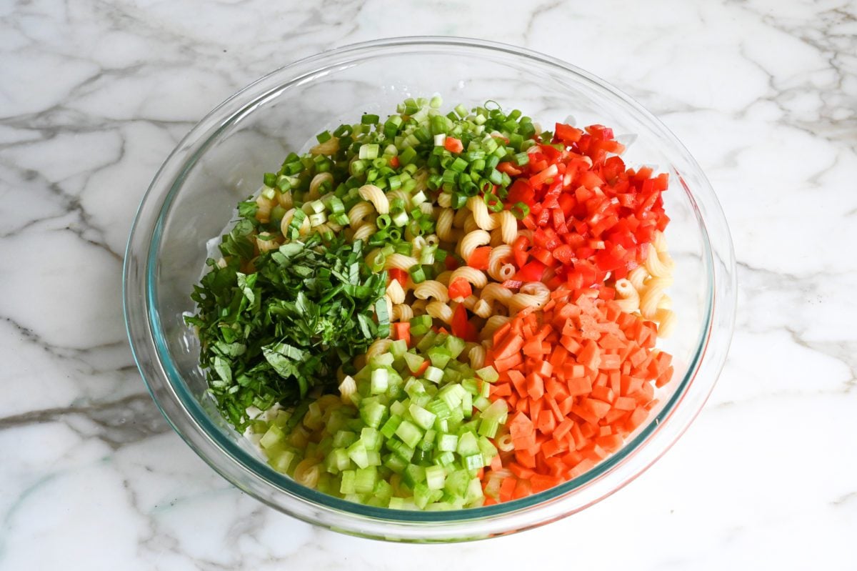 adding pasta, vegetables and basil to dressing