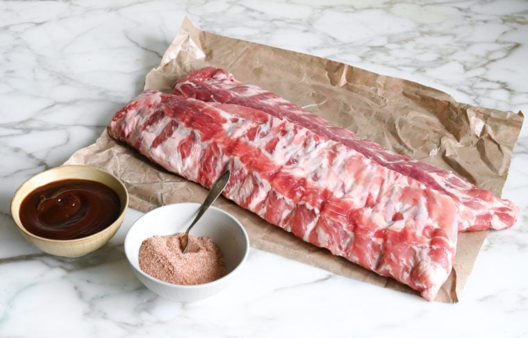Ribs, spices, and barbeque sauce on a countertop.