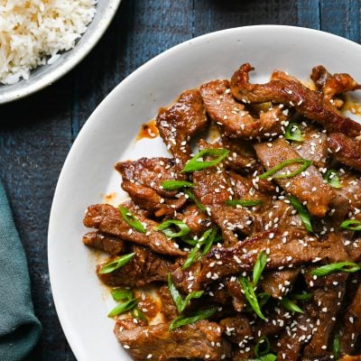 Beef bulgogi on platter with rice and hot sauce on the side.