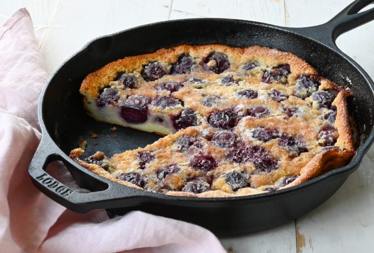 Partially sliced cherry clafoutis in a skillet.