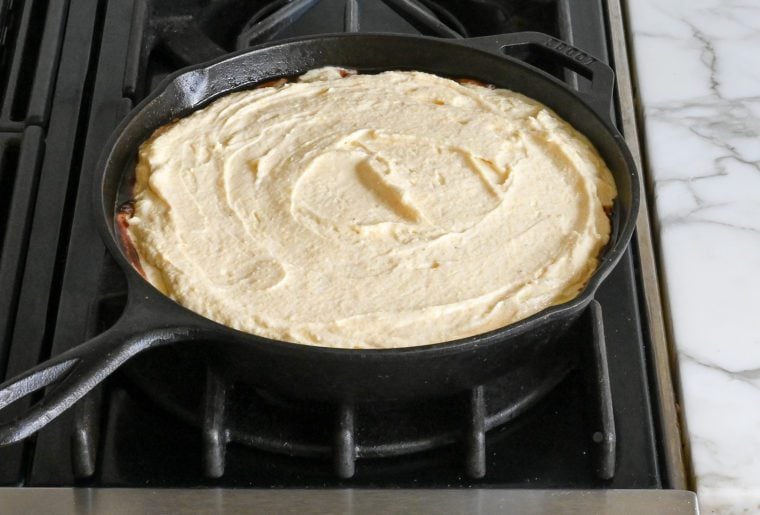 cake batter spread over cherries in skillet