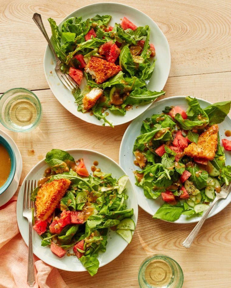 Table set with plates of salad and glasses of white wine.