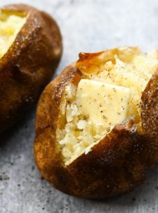 Two baked potatoes with butter on parchment paper.