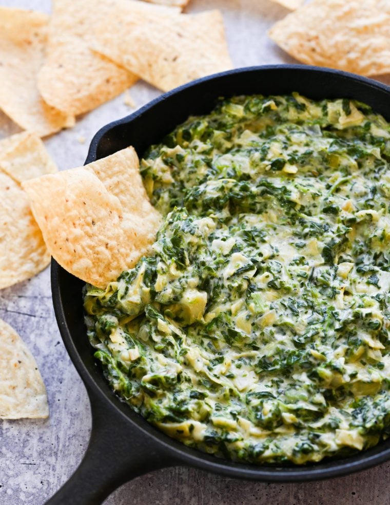 Tortilla chip in a bowl of spinach artichoke dip.