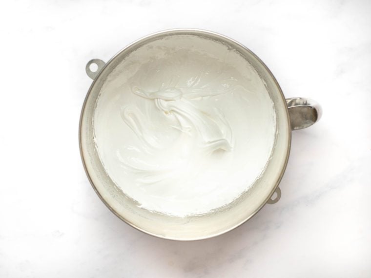 Egg-sugar mixture with medium peaks in a mixing bowl.