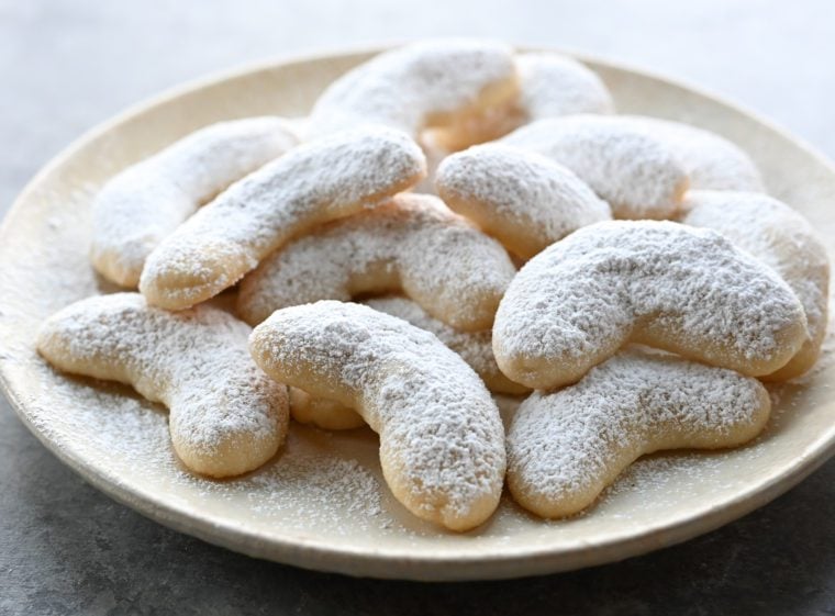 Snowball cookies shaped like crescents piled on a plate.