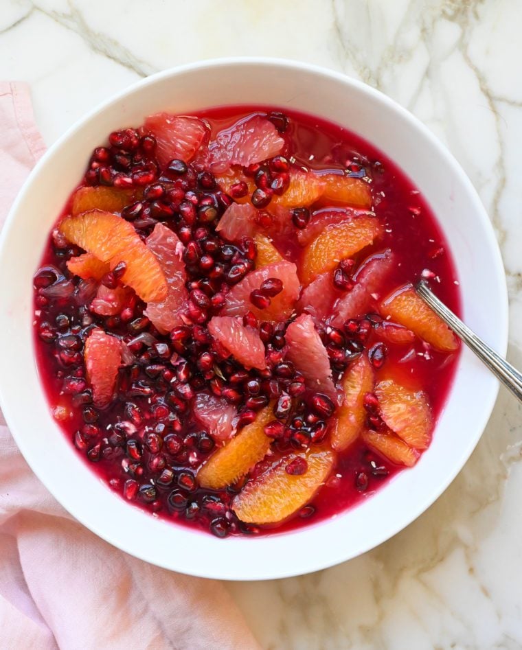 Spoon in a bowl of citrus and pomegranate fruit salad.