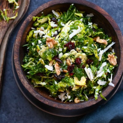 Wooden bowl of kale, brussels sprouts, and dried cranberry salad with honey-dijon vinaigrette.