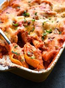 Spoon scooping cheesy stuffed shells from a baking dish.