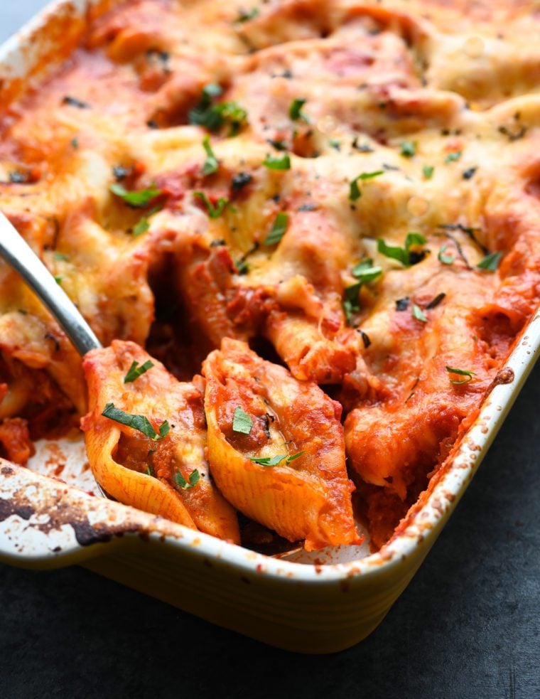 Spoon scooping cheesy stuffed shells from a baking dish.