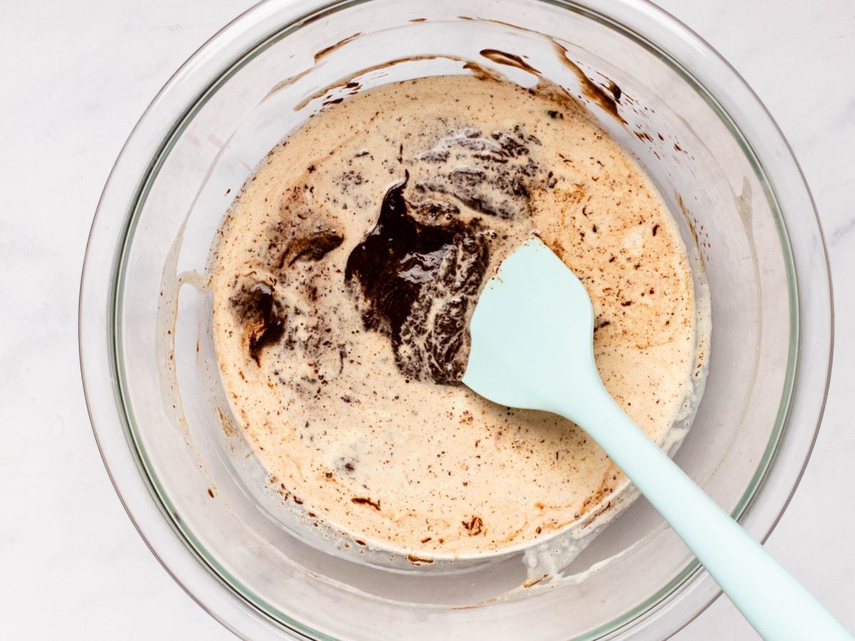 Spatula mixing heavy cream and melted chocolate in a glass bowl.