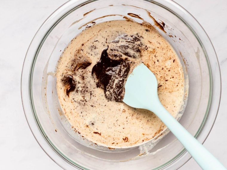 Spatula mixing heavy cream and melted chocolate in a glass bowl.