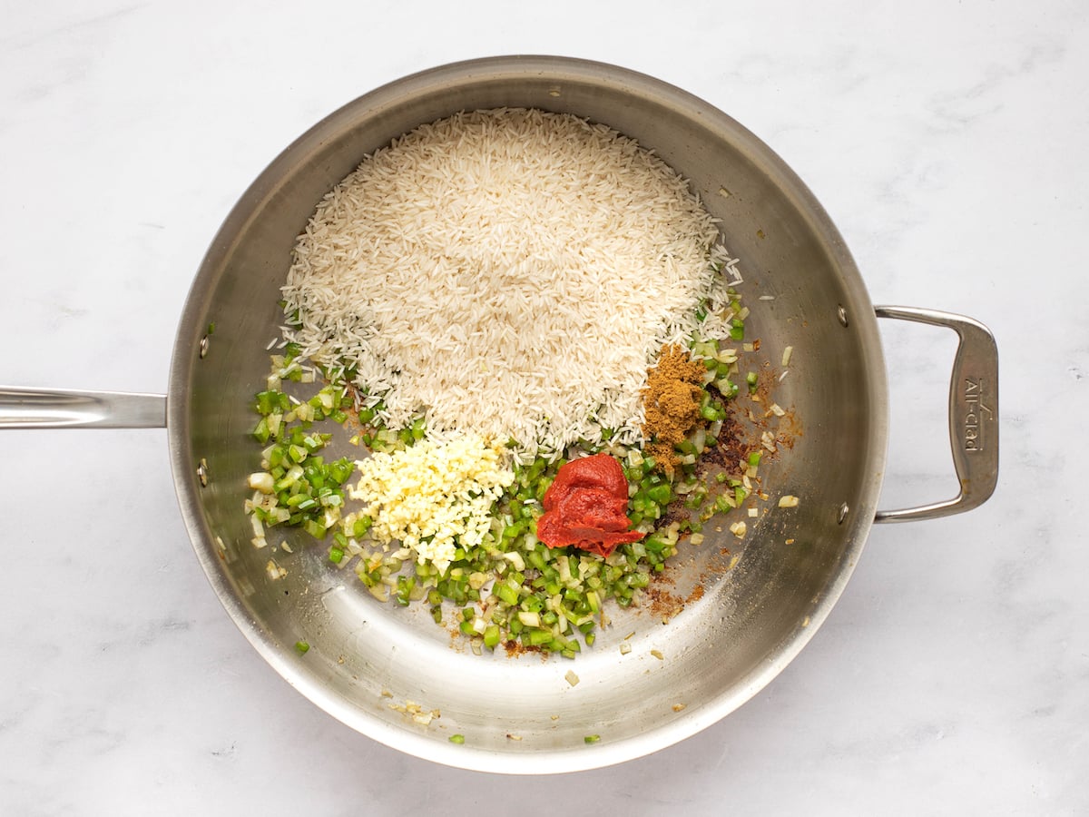 adding rice, garlic, tomato paste, and cumin to skillet