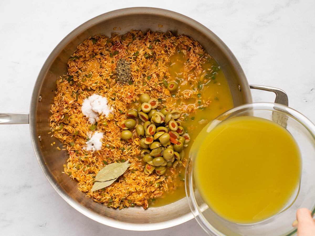 pouring broth into skillet for arroz con pollo