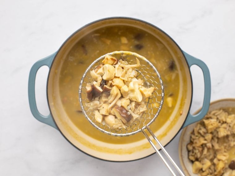 removing a few spoonfuls of mushrooms from soup