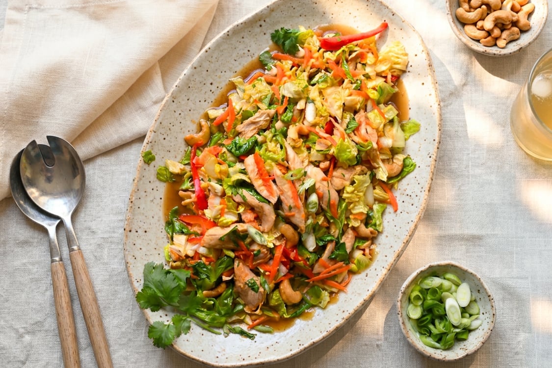 Chinese chicken salad on platter with small bowls of cashews and scallions